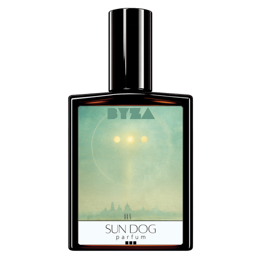 A rectangular perfume bottle with a glossy black cap and a front label reading 'BYZA' and 'SUN DOG parfum'. The label artwork shows a pale teal sky with a bright sun and a silhouetted city skyline.